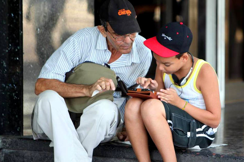 Dos personas navegan por la internet en un dispositivo móvil, en una de las zonas habilitadas con Wifi en La Habana (Cuba). Los cubanos navegan por internet en móviles y "tablets" a lo largo de La Rampa, una de las principales avenidas de la capital, una estampa nada habitual en Cuba pero que ya es posible en los nuevos espacios wi-fi habilitados esta semana en 35 zonas públicas de la isla. Ernesto Mastrascusa EFE